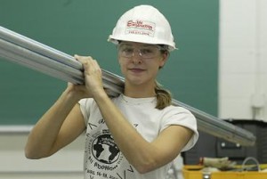 Female electrician wearing a hard hat caring a long metal tube on her shoulder