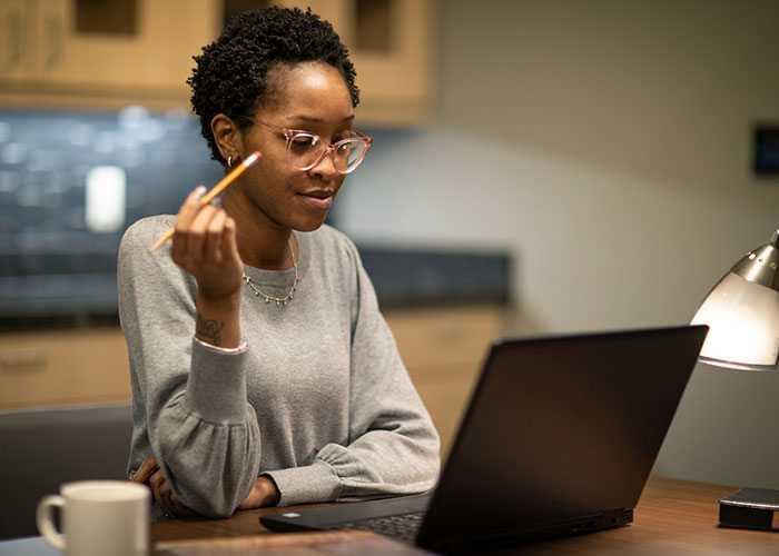 Student holding pencil watch an online class on a laptop.