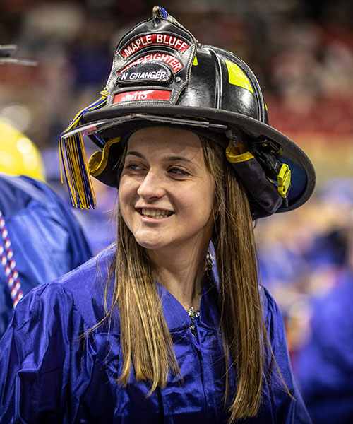 Madison College graduate wearing a firefighter's helmet